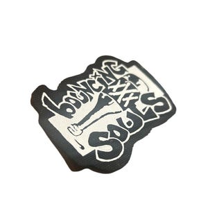 May include: Black and white sticker with the text "Lounging Soles" in a stylized font. The sticker features a graphic of a person's leg wearing a shoe.