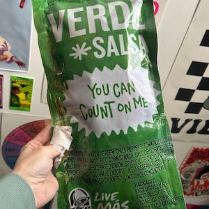 Op de afbeelding: Een groene plastic zak met Taco Bell Verde *Salsa* met de tekst "You Can Count On Me" en "Live Mas".