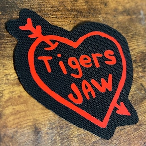 May include: Red heart-shaped patch with a red arrow on each side. The words "Tigers Jaw" are written in red inside the heart.