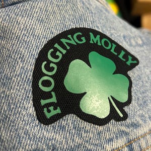 May include: A black patch with a green four-leaf clover and the text "FLOGGING MOLLY" in white.