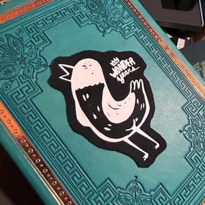 May include: A teal blue book with a gold border and a black and white patch of a bird with the text "My Wonder Years" on it.