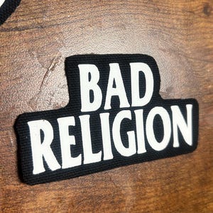 Op de afbeelding: Zwart-witte geborduurde patch met de tekst "BAD RELIGION" in witte letters.