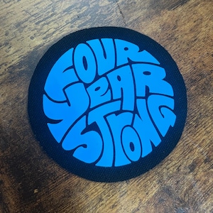 May include: A black and blue circular patch with the text "Four Year Strong" in a stylised font.