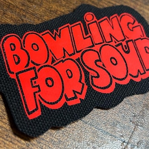 Pode incluir: Um remendo de tecido preto com letras vermelhas que dizem "Bowling For Soup".