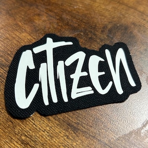 May include: Black fabric patch with the word "CITIZEN" written in white, stylized lettering.