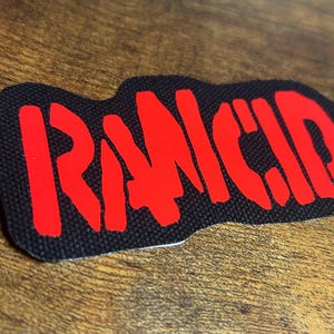 May include: A black fabric patch with the word "RANCID" in red lettering.