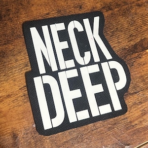 Op de afbeelding: Zwarte stoffen patch met witte tekst "Neck Deep".
