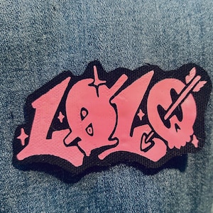 Pode incluir: Patch bordado rosa e preto com a palavra "LOVE" em uma fonte de estilo graffiti com um coração e uma flecha.