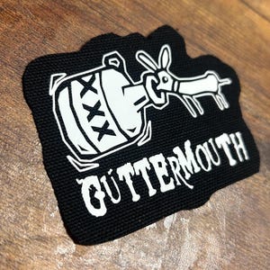 May include: Black and white embroidered patch with a cartoon dog drinking from a bottle labeled "XXX". The text "GUTTERMOUTH" is below the image.