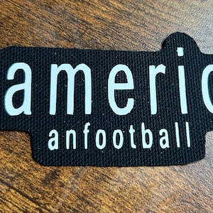 May include: Black fabric patch with white text that reads "americ anfootball".