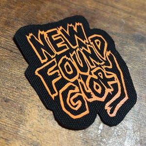 May include: Black fabric patch with the words "NEW FOUND GLORY" in orange outlined lettering.