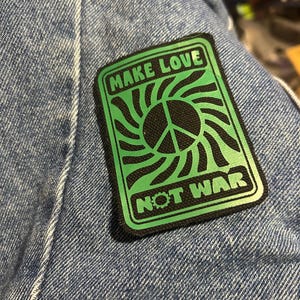 May include: A green and black patch with a peace sign and the text "Make Love Not War".