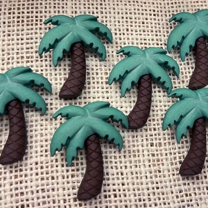 May include: A set of six green and brown palm tree buttons. The buttons are made of plastic and have a 3D design.