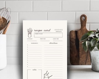 May include: A printable recipe card template with a black and white illustration of kitchen utensils. The card has sections for the name of the dish, category, prep time, cook time, ingredients, directions, and notes.