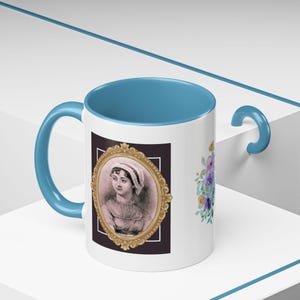 May include: White ceramic mug with a blue rim and handle. The mug features a portrait of Jane Austen in a gold frame with floral accents on the side.