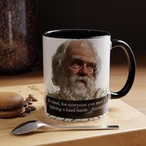 May include: White ceramic mug with a black rim and handle. The mug features a portrait of Socrates with a quote: "Be kind, for everyone you meet is fighting a hard battle - Socrates".