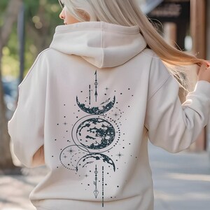 May include: A cream-colored hoodie with a black and white moon phase design on the back. The hoodie has a drawstring hood and a kangaroo pocket.