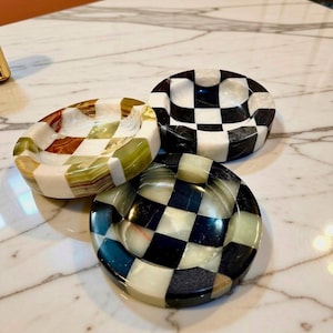 May include: Three circular stone trays featuring a checkerboard pattern. One tray displays white and green marble tones, while the other two trays exhibit a high-contrast black and white checkered design with a polished, smooth finish.