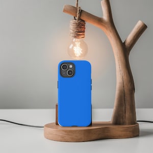 May include: A bright blue phone case with a camera lens cutout sits on a wooden stand with a light bulb hanging above it.