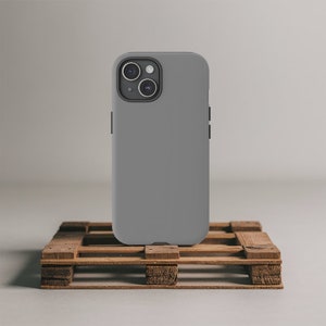 May include: A gray smartphone case with a dual-lens camera is displayed. The case is a solid, matte gray color. The phone case is resting on a small, wooden pallet.