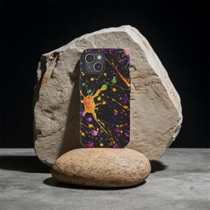 May include: A black phone case with a colorful paint splatter design. The case has a camera cutout and a black background. The paint splatters are in shades of yellow, purple, green, and blue.