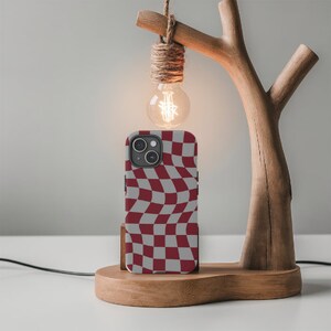 May include: A red and white checkered phone case with a wavy pattern. The case is on a wooden stand with a light bulb hanging above it.