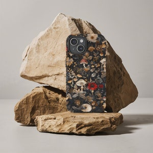 May include: A black phone case with a floral and mushroom design. The case features a variety of mushrooms, flowers, and leaves in shades of red, white, and brown.