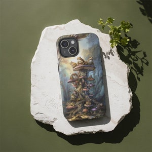 May include: A phone case with a colorful illustration of a mushroom tower with frogs sitting on top. The background is a forest scene with a soft, dreamy feel.