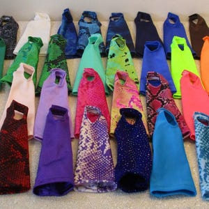 Puede incluir: Una colección de tops sin mangas coloridos, en varios colores lisos y estampados. Los tops están dispuestos sobre una superficie clara, mostrando una diversa gama de tonos, incluyendo azul, verde, rosa y diseños estampados. Los tops parecen ser de tela.