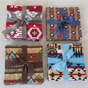 May include: Four sets of square fabric coasters with Southwestern patterns, each tied with a ribbon. The coasters feature red, tan, and blue designs with geometric and tribal motifs. Each set is approximately 4 inches square.