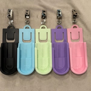 May include: Five different colored plastic badge holders with a clip on top. The holders are black, light blue, light green, purple, and pink.