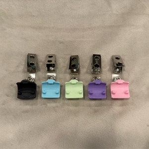 May include: Six retractable badge holders with different colored plastic covers. The covers are black, light blue, light green, purple, and pink.