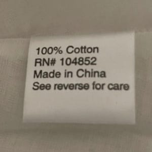 May include: A white rectangular tag with black text. The text reads "100% Cotton", "RN# 104852", "Made in China", and "See reverse for care". The tag is likely a clothing label.