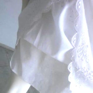 May include: A white garment with a scalloped edge and embroidered floral details. The fabric appears to be lightweight and flowing, with a soft, textured appearance. The design suggests a delicate, feminine aesthetic.