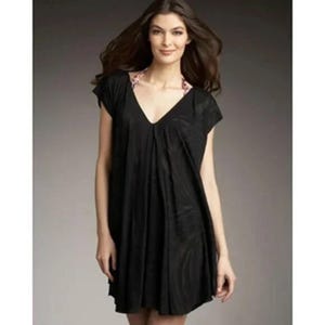 May include: A black, short-sleeved dress with a deep V-neckline. The dress has a loose, flowing silhouette and a patterned trim around the neckline. The fabric appears to have a subtle texture. The dress is knee-length.