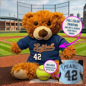 May include: A plush brown teddy bear wearing a navy blue jersey with the word "Softball" and the number 42. A yellow softball sits in front of the bear. The image includes text that says "Full Color Printing" and "Includes Personalization".