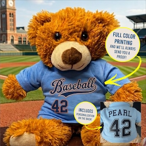 May include: A plush brown teddy bear wearing a light blue baseball jersey with the word "Baseball" and the number "42" printed on the front. The jersey includes personalization on the back. The bear has a brown snout and dark eyes.