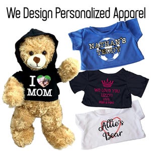 May include: A plush teddy bear wearing a black hoodie with "I MOM" printed on it, and three personalized t-shirts. One blue shirt says "NATHAN'S TEDDY", a black shirt says "We love you Lizzy!", and a white shirt says "Allie's Bear". The text "We Design Personalized Apparel" is at the top.