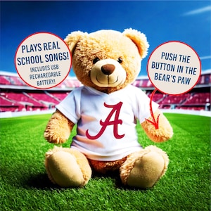 May include: A plush teddy bear wearing a white t-shirt with a maroon "A" logo. The bear is sitting on green grass with a stadium in the background. Text on the image says "Plays Real School Songs!" and "Push the button in the bear's paw."