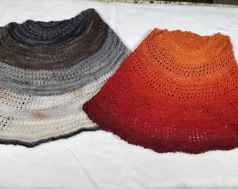 Può includere: Due scialli lavorati a maglia. Uno è un gradiente di blu scuro, marrone, grigio e crema. L'altro è un gradiente di rosso, arancione e giallo. Entrambi gli scialli hanno un bordo smerlato e un motivo traforato.
