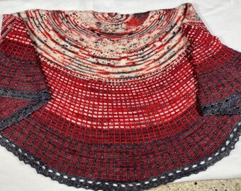 Può includere: Uno scialle lavorato a mano a maglia nei toni del rosso, bianco e grigio. Lo scialle presenta un motivo sfumato, che passa da un rosso intenso in basso a tonalità più chiare in alto. I bordi sono rifiniti con un bordo grigio smerlato.