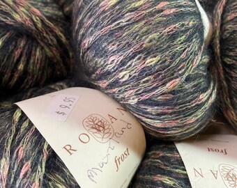 Può includere: Primo piano di un gomitolo di lana in una combinazione di colori nero, verde e rosa. La lana è etichettata "Rowan Mountain Frost" e ha un cartellino del prezzo di 9,95 €.
