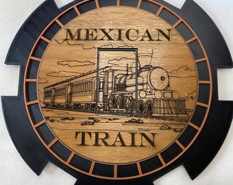 Può includere: Un cartello rotondo in legno con un bordo nero e arancione. Il cartello presenta un'illustrazione in bianco e nero di un treno con le parole "MEXICAN TRAIN" in lettere nere.