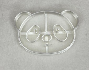 Può includere: Un tagliapasta in plastica bianca a forma di viso di panda. Il tagliapasta ha un design dettagliato con occhi, naso e bocca.
