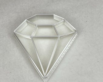 Può includere: Un vassoio di plastica trasparente a forma di diamante con più scomparti. Il vassoio è progettato per contenere piccoli oggetti come gioielli o altri gingilli.