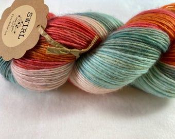 Può includere: Un gomitolo di filato tinto a mano in un motivo a spirale multicolore. Il filato è una miscela di colori rosa, arancio e turchese. Il filato è etichettato "SWIRL" con un'etichetta che dice "Sweet 2 Yarn" e "A Five Color Set".