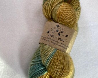 Può includere: Un gomitolo di filato tinto a mano in tonalità giallo senape e verde acqua. Il filato è avvolto attorno a un'etichetta di carta marrone che recita "ewe 2 yarn" e include il testo "Hand Dyed-Nature Inspired-Eco-Friendly Yarns ewe2yarn.com instagram.com/ewe2yarn"