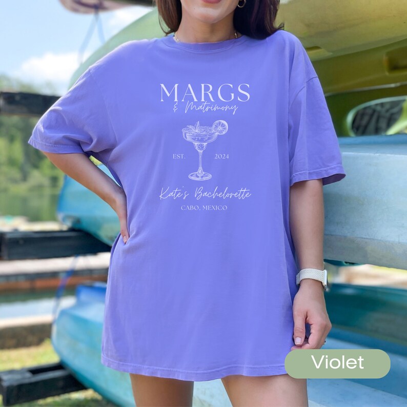 May include: A purple t-shirt with the text "MARGS & Matrimony Est. 2024 Kate's Bachelorette Cabo, Mexico" and a margarita glass graphic.