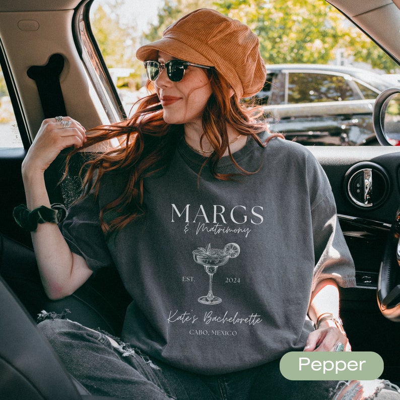 May include: A gray t-shirt with the text "MARGS & Matrimony" and a margarita illustration. The text "EST. 2024" and "Kate's Bachelorette Cabo, Mexico" are also printed on the shirt.