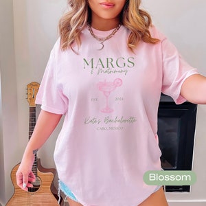 May include: Pink t-shirt with a margarita graphic and the text "MARGS & Matrimony Est. 2024 Kate's Bachelorette Cabo, Mexico" printed on the front.